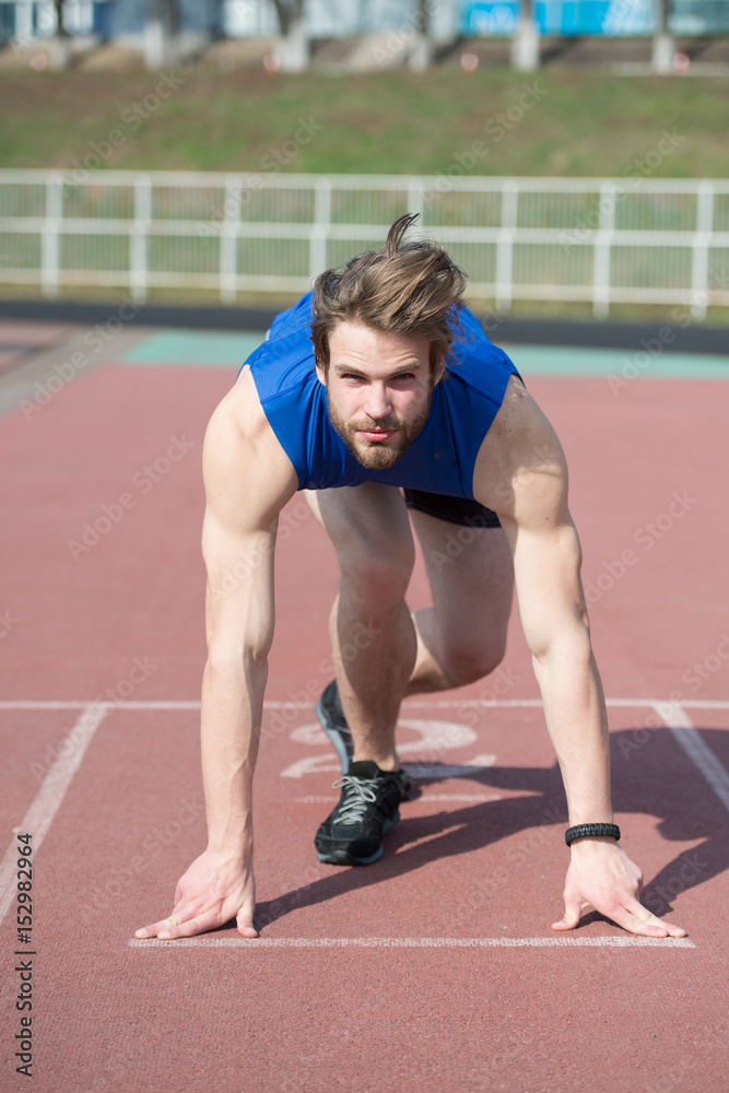 athletic bearded man with muscular body stretching on running track