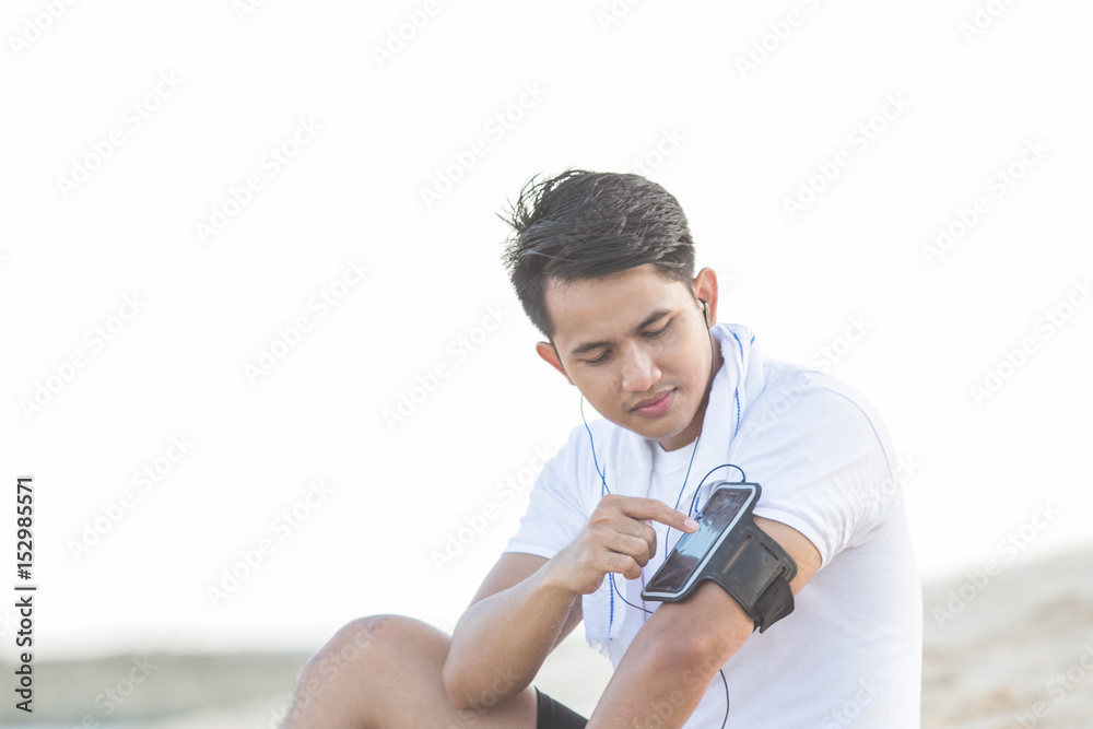 sport man relaxing sitting on a sand while listening music sport man relaxing sitting on a sand while listening music