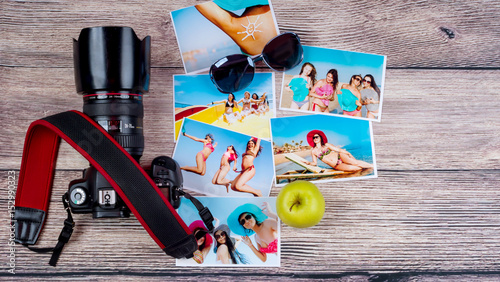 Top view of a lot of photos of cheerful beautiful girls in bathing suits next to a professional camera over a wooden background
