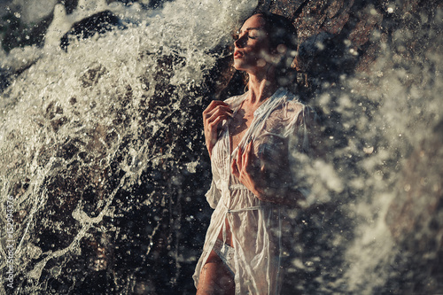 Young woman in white shirt and bikini stands in water flows near