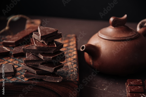 Whole and slices of dark chocolate on a wooden board in Monochrome setting. Toned. photo