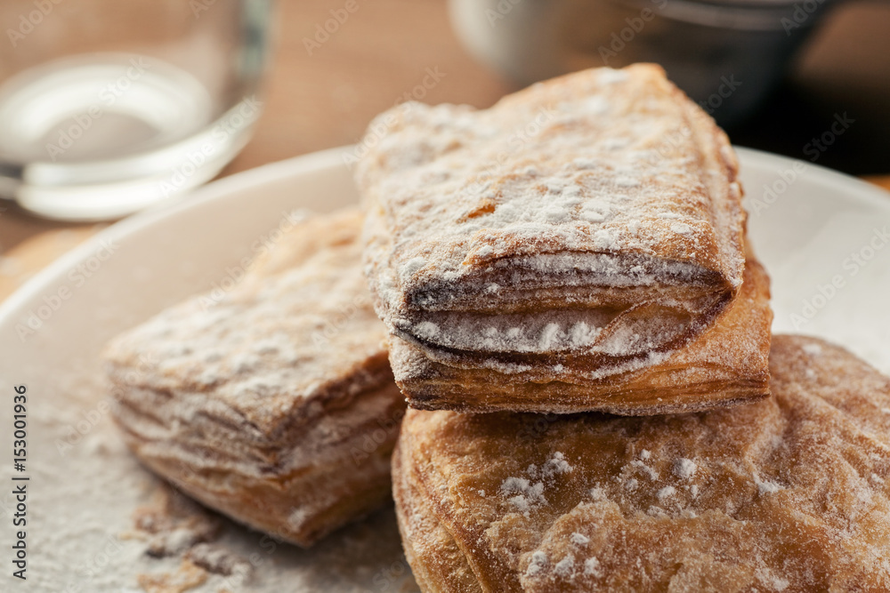 Puff pastry dusted with powdered sugar in a white plate, macro shot