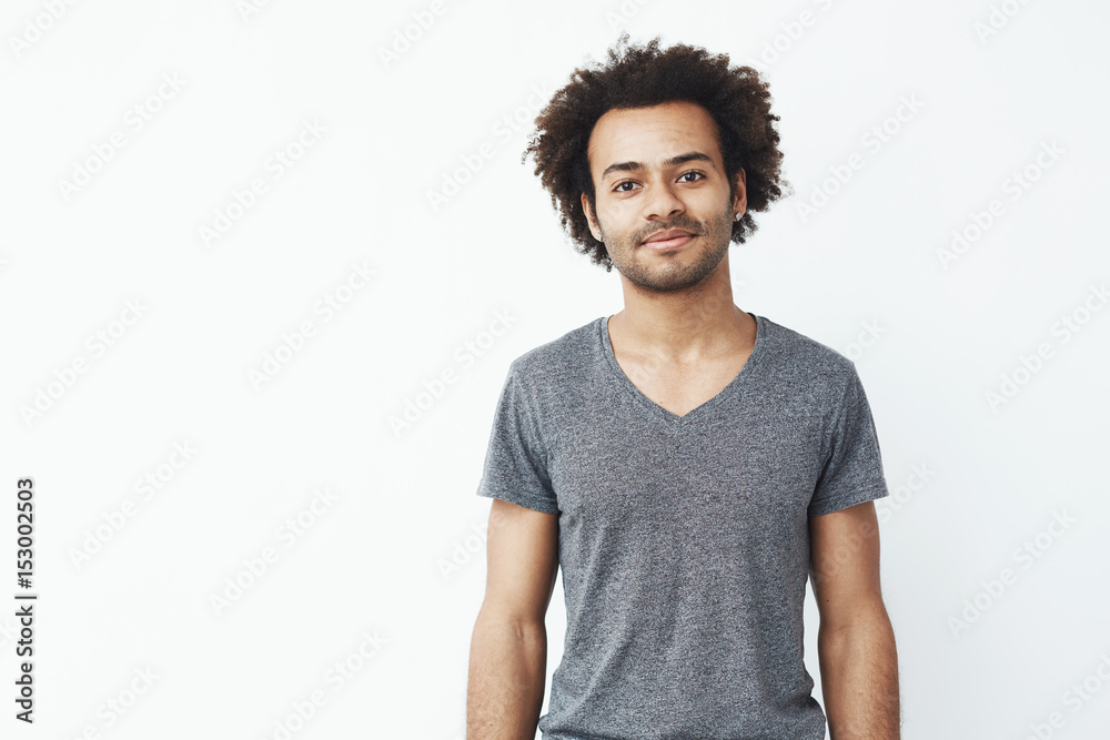 Portrait of stong and handsome african man smiling looking at camera posing over white wall. Confident student or shop owner. Portrait of stong and handsome african man smiling looking at camera posing over white wall. Confident student or shop owner.