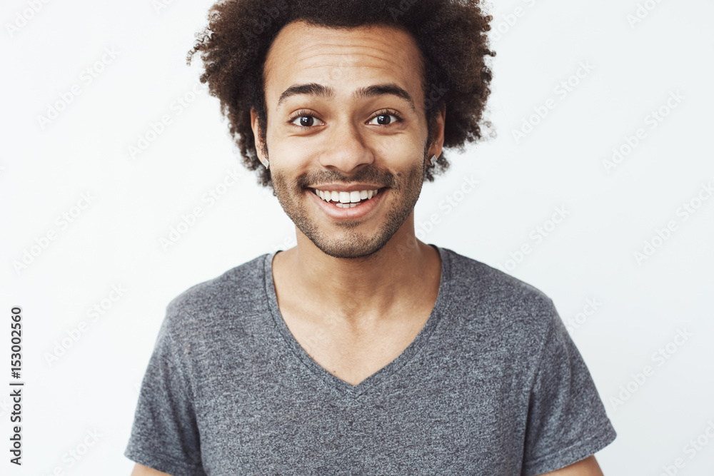 Close up portrait of happy and charming african guy smiling at camera, a boyfriend waiting for a date, or a head hunter dream standing over white wall.