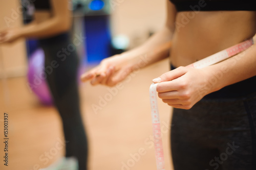 Young slim woman measuring waist using the tape measure.