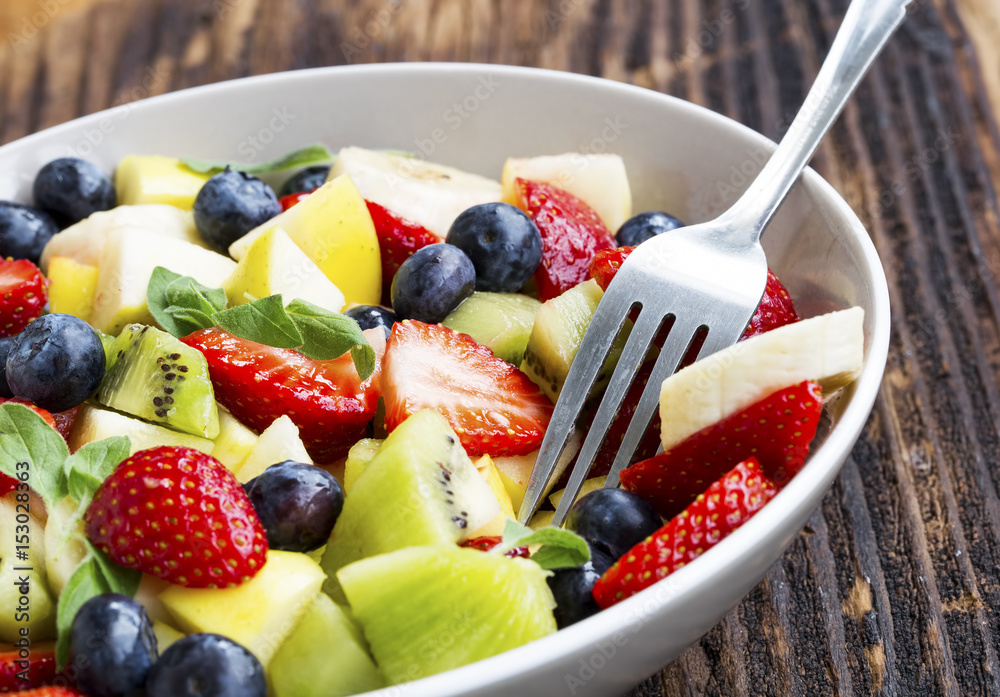 Bowl of fruits salad with strawberries, blueberries, apples, kiwi, bananas in slices, healthy seasonal summer fruits salad assortment