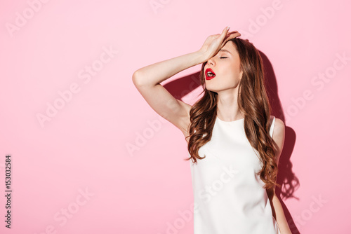 Portrait of annoyed beautiful woman placing back hand on forehead photo