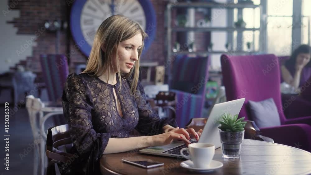 Lovely female with laptop in cafe. Beautiful female with cup of coffee sitting in cafe and using laptop.