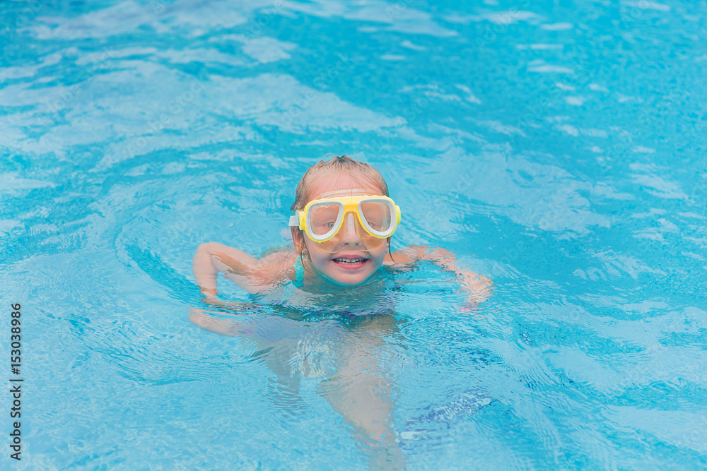 Cute happy young girl child relaxing on the side of swimming pool wearing pink goggles