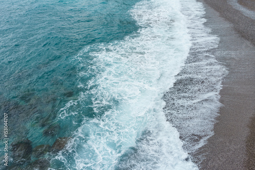 Soft and gentle blue sea waves foam in italy stone sand coast shore in summer daylight.