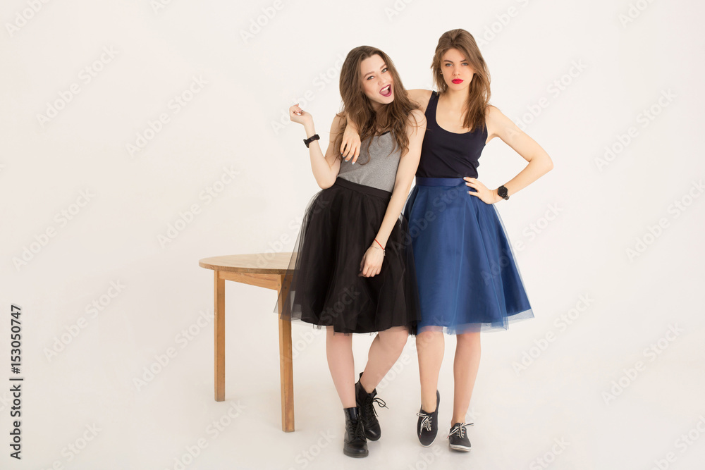 Rock and roll girls fooling around next to a wooden table isolated. Cheerful emotional best girlfriends rocking wearing skirts and dark lipstick