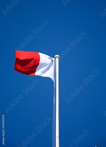 The Maltese flag atop a flagpole in Castille Square against a blue sky  Valletta  Malta.