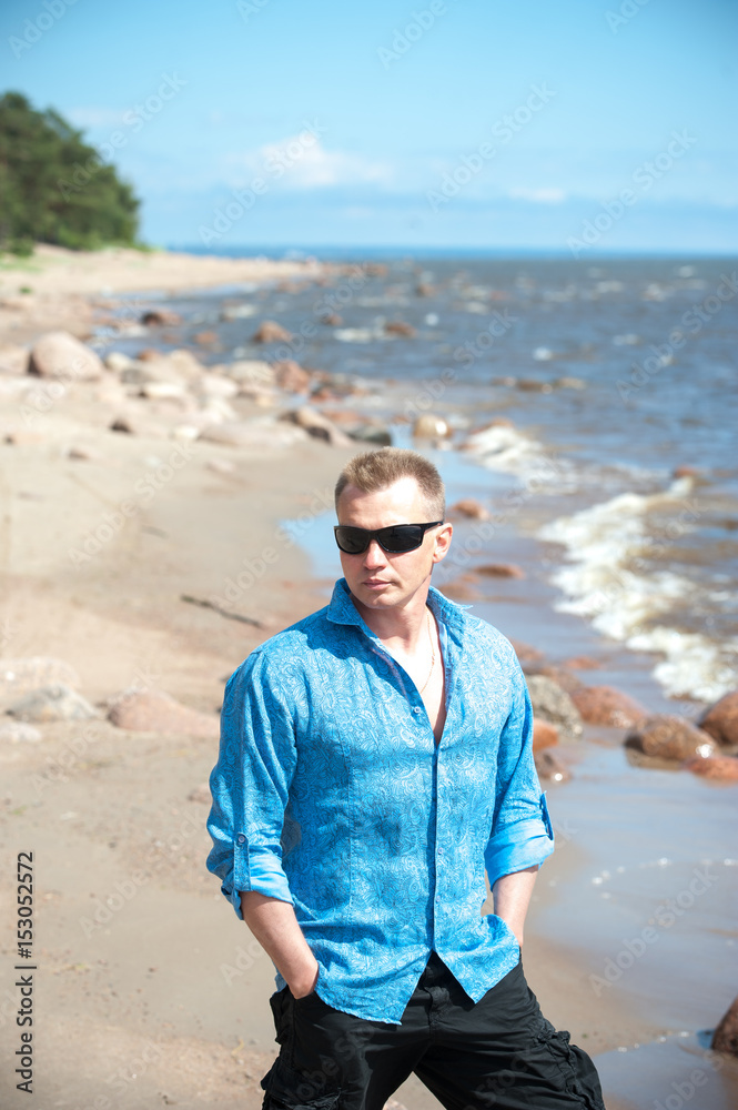 A young man, a guy in an open blue shirt on a summer day's beach
