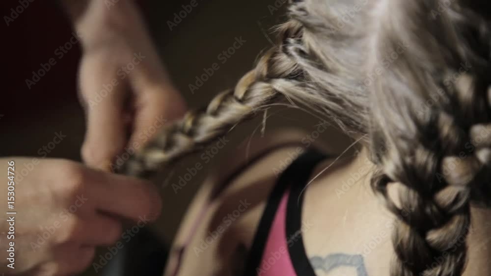 Hairdresser styling makes styling easier, plaiting braids for young brunette woman in a beauty salon
