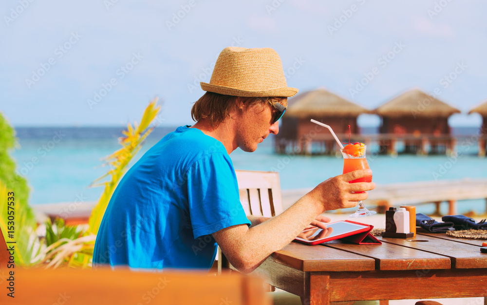 youg man drinking cocktail looking at touch pad on beach resort