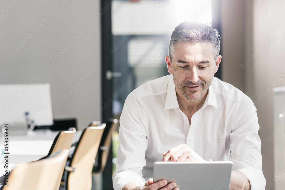 Smiling businessman sitting in his conference room using tablet Smiling businessman sitting in his conference room using tablet