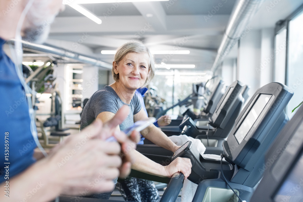 Group of fit seniors on treadmills working out in gym, woman smiling Group of fit seniors on treadmills working out in gym, woman smiling