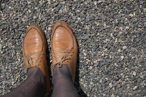 Female legs in brown shoes on a background of gravel