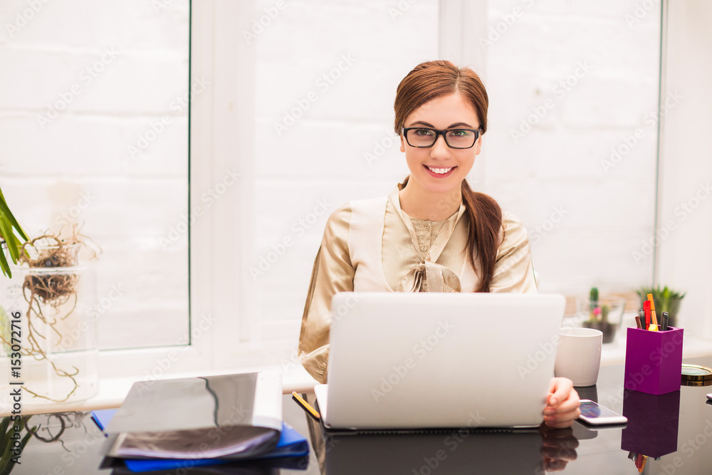 Young cheerful business woman sits at the table with laptop and folders at the office Young cheerful business woman sits at the table with laptop and folders at the office
