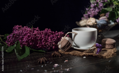 Coffee and cream macarons with cup of coffee and lilac on background