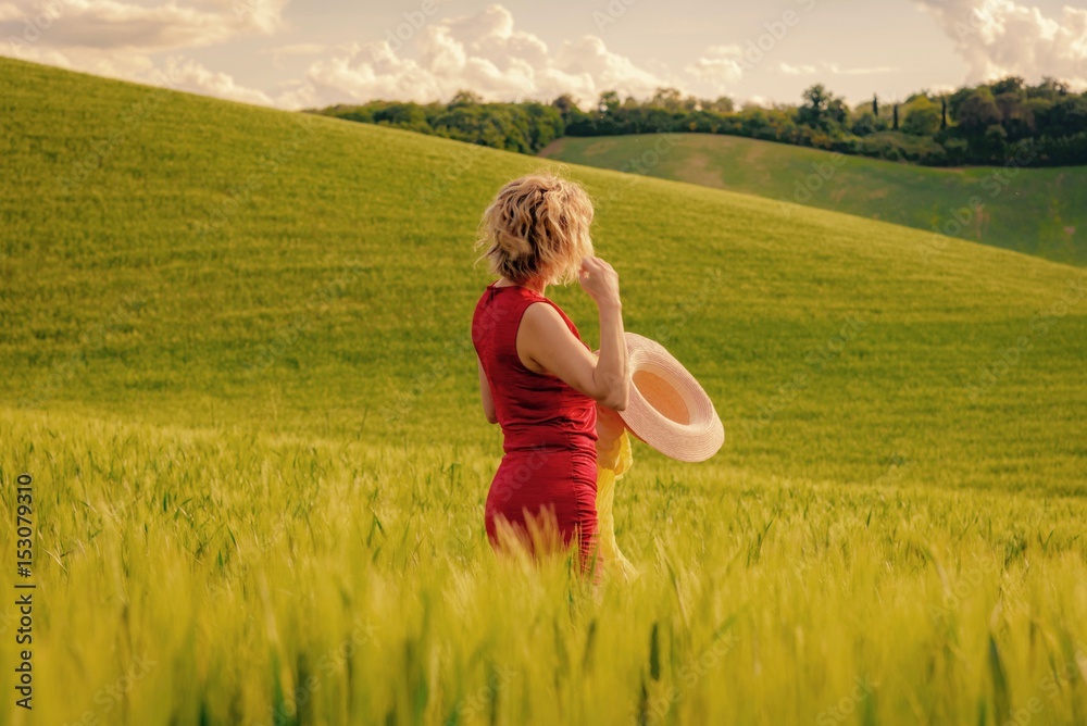 Woman with red dress on hay hills in italy in spring