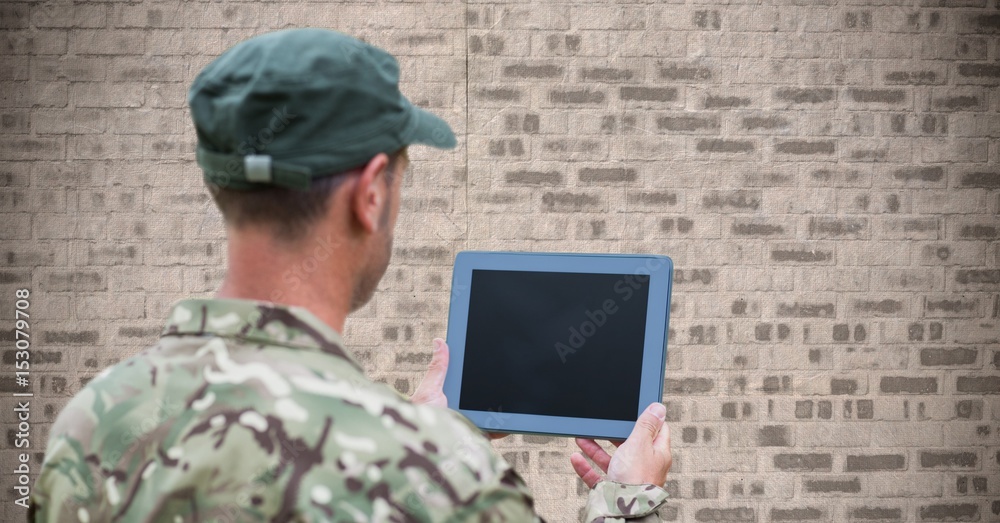 Back of soldier with tablet against brown brick wall