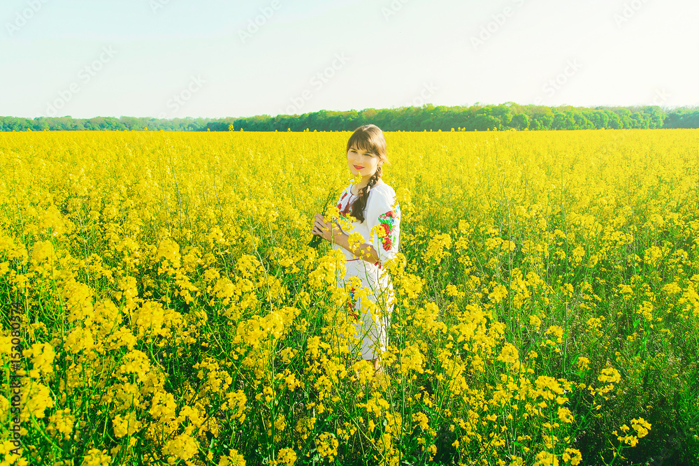Beautiful young woman in Ukrainian embroidered standing in a field of yellow rape flowers Beautiful young woman in Ukrainian embroidered standing in a field of yellow rape flowers
