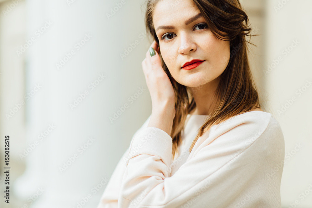 Close up portrait of elegant woman with red lips in a beige blouse on the white building background. Close up portrait of elegant woman with red lips in a beige blouse on the white building background.
