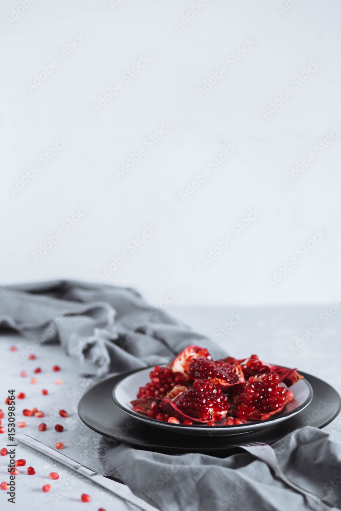 pieces of pomegranate in a bowl on grey kitchen towel with candles on white background romantic table