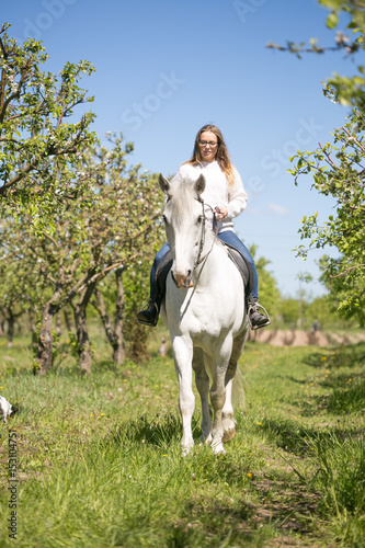 Beautiful girl riding a horse on a white horse in the garden