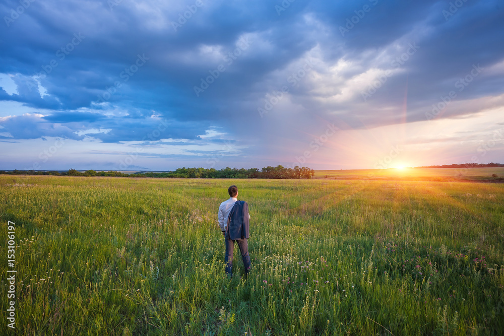 Fototapeta premium businessman in a suit walking on a spacious green field with a blue sky