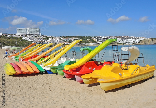 Fototapeta Naklejka Na Ścianę i Meble -  Group of colorful pedal boats with and without slide on the beach of Arenal d'en Castell, Menorca Island, Spain.