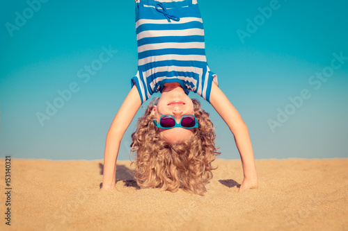 Funny child standing upside down on sandy beach