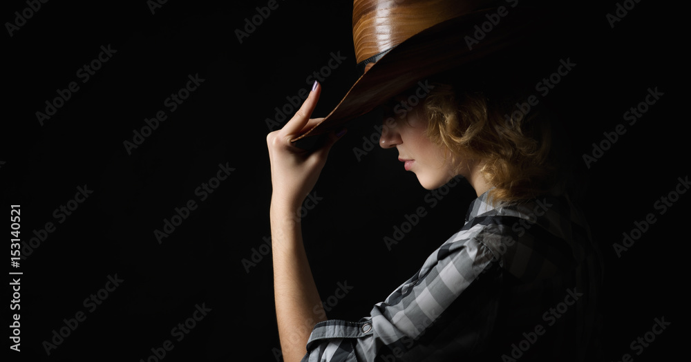 Beautiful girl in a cowboy's hat isolated on black background .
