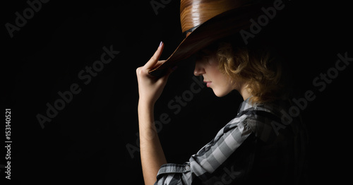 Beautiful girl in a cowboy s hat isolated on black background .
