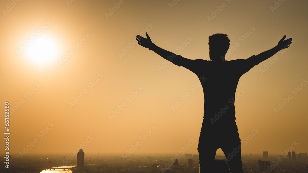 Man standing at the edge of rooftop, stretching arms. Sunset on cityscape background Freedom or success concept. Copy space. Purple color tone.