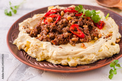 Creamy hummus with spicy mutton minced meat in clay bowl on stone background. Ramadan food.