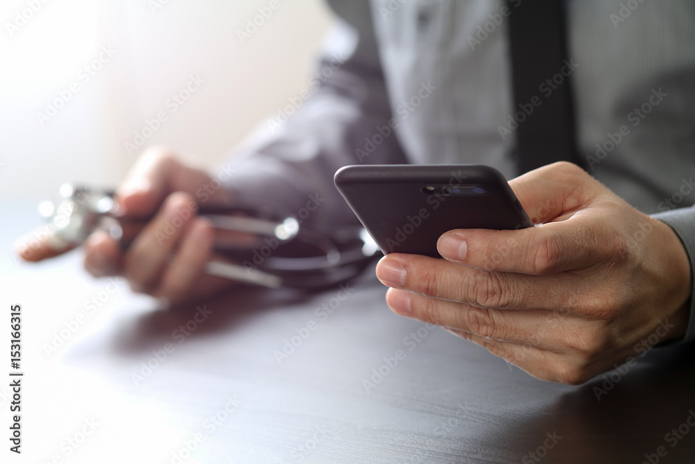 close up of smart medical doctor working with mobile phone and stethoscope on dark wooden desk close up of smart medical doctor working with mobile phone and stethoscope on dark wooden desk