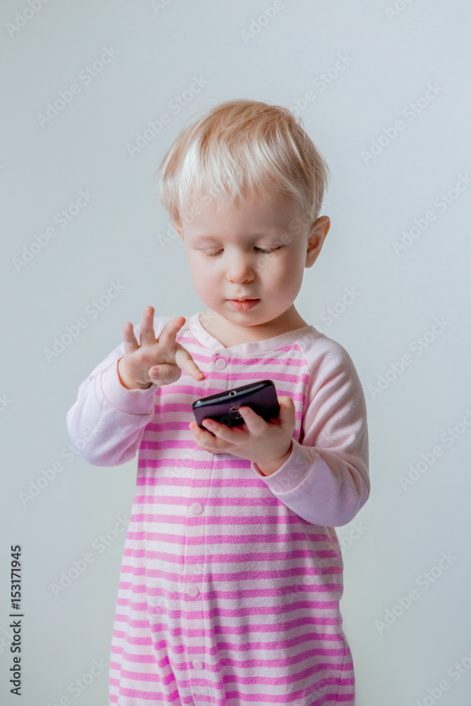 Cute adorable white Caucasian blond baby with blue eyes making a call, playing with mobile cell phone with funny expression on her face, lifestyle new generation technology Cute adorable white Caucasian blond baby with blue eyes making a call, playing with mobile cell phone with funny expression on her face, lifestyle new generation technology