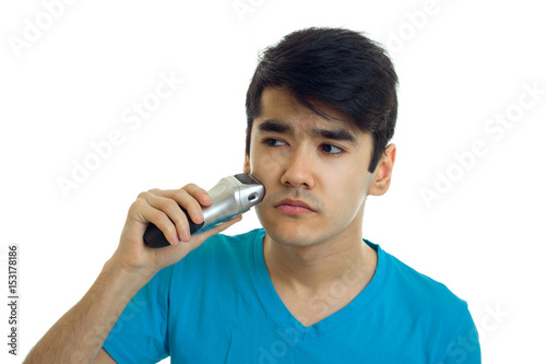 young strong guy in a t-shirt looking sideways and shaves a beard trimmer is isolated on a white background