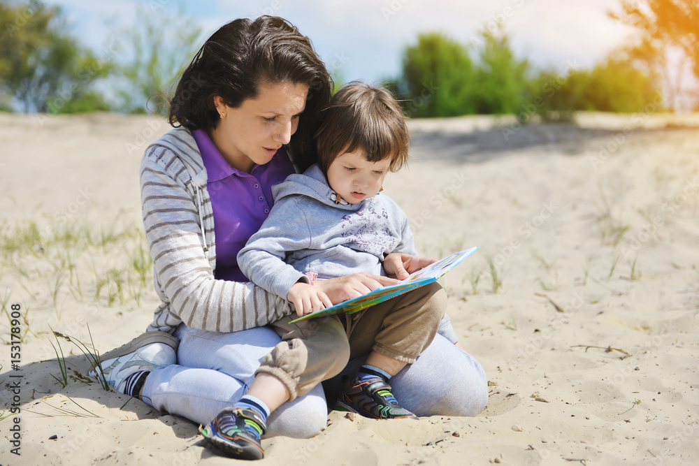 Woman with a toddler reading a book on the beach. Woman with a toddler reading a book on the beach.