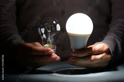 Female hands holding a glowing led and incandescent bulbs in the dark