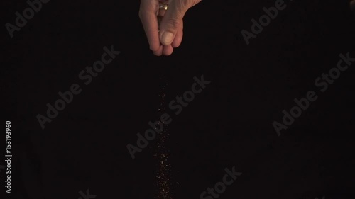 A hand of caucasian man pouring spices on black background, slow motion HD photo