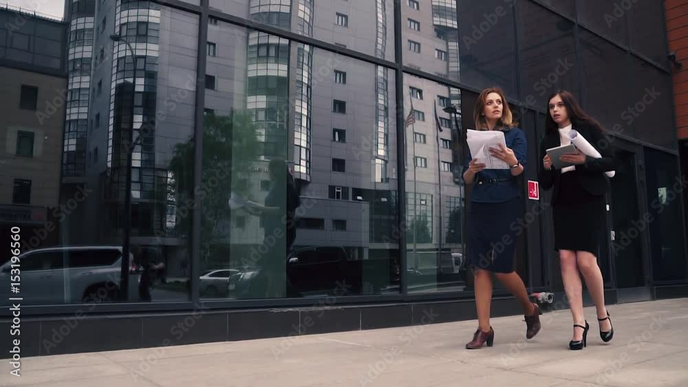 confident business woman walking in the background of a modern business center. girl holding blueprints and talking on the go. women in business clothes on the street. Slow Motion confident business woman walking in the background of a modern business center. girl holding blueprints and talking on the go. women in business clothes on the street. Slow Motion