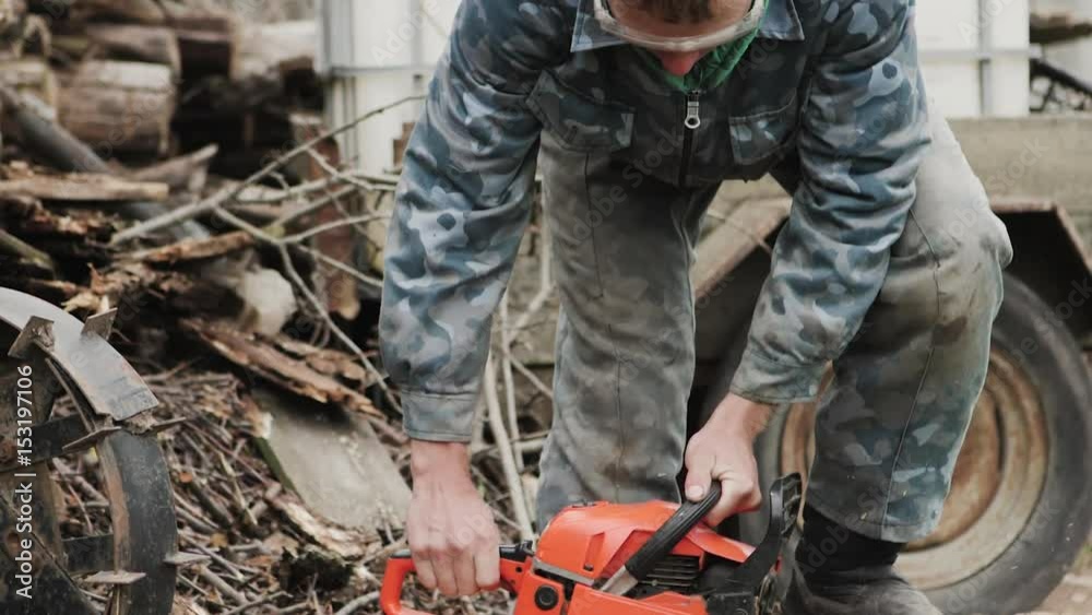The man is sawing firewood with a chainsaw. Woodcutter in special headphones and goggles. Slow Motion The man is sawing firewood with a chainsaw. Woodcutter in special headphones and goggles. Slow Motion