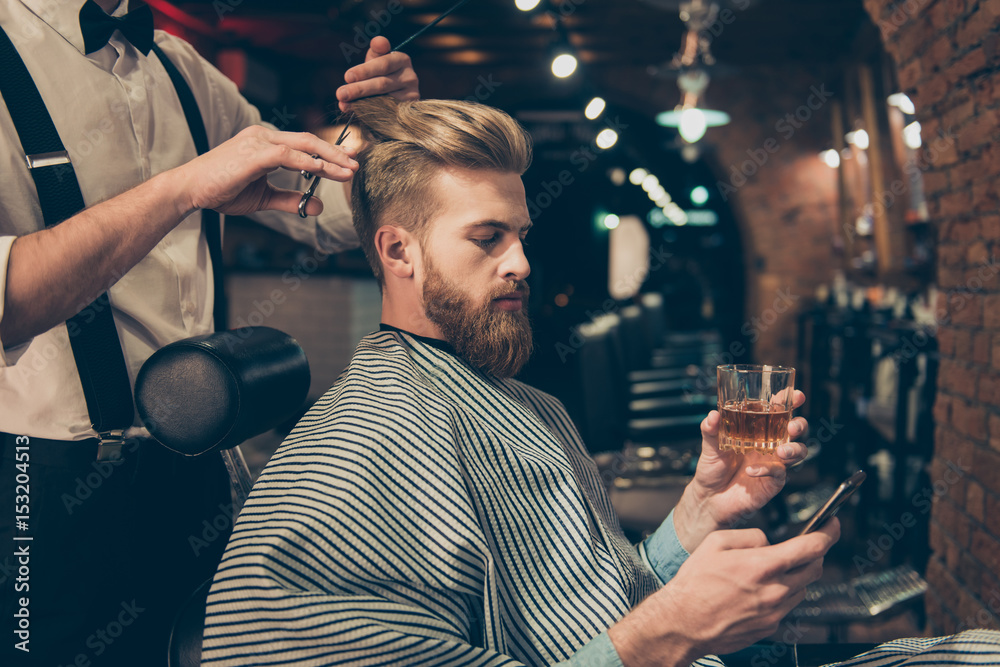 Chill out at the barber shop. Side view of handsome young red bearded man drinking scotch and