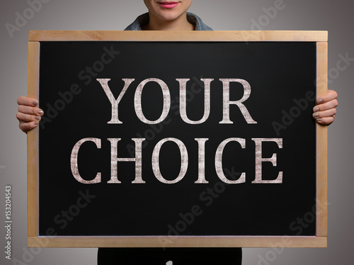 Girl (student, businesswoman) in casual clothes holding a black chalk board with text YOUR CHOICE