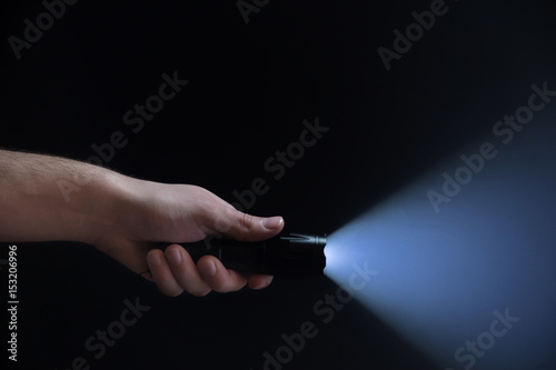 Black flashlight with wide beam in male's hand isolated from right side of the frame on black background