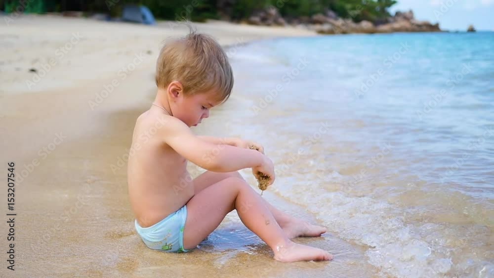 The child is sitting on the beach, swims in the sea waves in a Sunny day. The child is sitting on the beach, swims in the sea waves in a Sunny day.