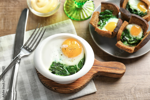 Bowl with tasty egg and spinach on wooden table